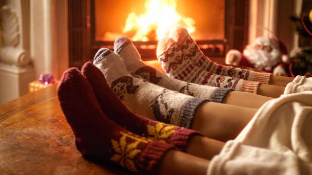 Foto de close-up de pais com criança em meias de lã aquecendo à noite pela lareira
 - Foto, Imagem