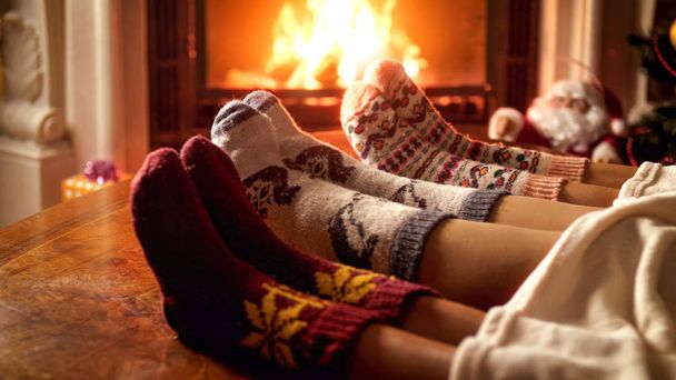 Family in warm knitted socks lying on sofa next to burning fireplace - Photo, Image