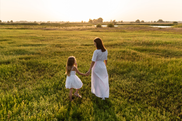 takana näkymä äiti ja tytär kävely vihreällä niityllä illalla
 - Valokuva, kuva