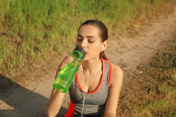 Σπορ νεαρή γυναίκα πόσιμου νερού μετά από να τρέξει στο πάρκο - Φωτογραφία, εικόνα