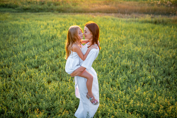 μεγάλη γωνία προβολής μητέρα και κόρη αγκαλιάζει το πράσινο λιβάδι στο ηλιοβασίλεμα - Φωτογραφία, εικόνα