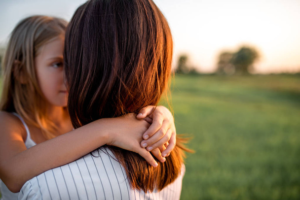 mother and daughter embracing in green meadow on sunset - Fotografie, Obrázek