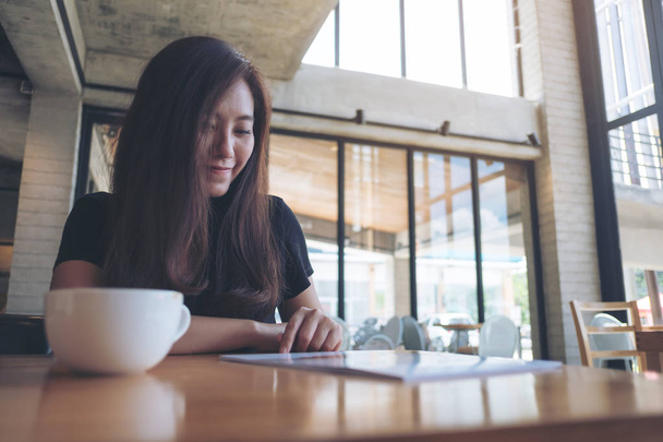 Image rapprochée d'une belle femme asiatique lisant un livre avec tasse à café blanche sur une table en bois dans un café moderne
  - Photo, image