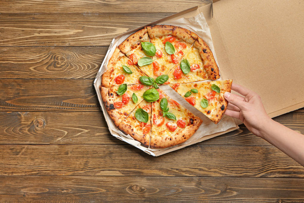 Młoda kobieta biorąc kawałek pyszne pizza Margherita z pudełko kartonowe na stole - Zdjęcie, obraz