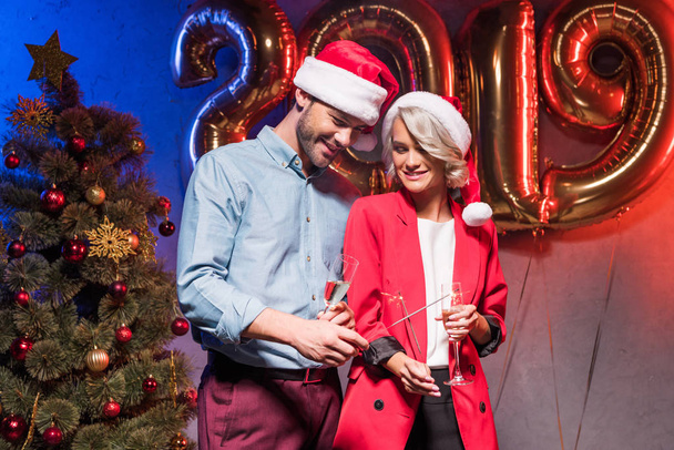 young businesspeople in santa hats holding glasses of champagne and christmas sparklers at new year corporate party - Foto, imagen