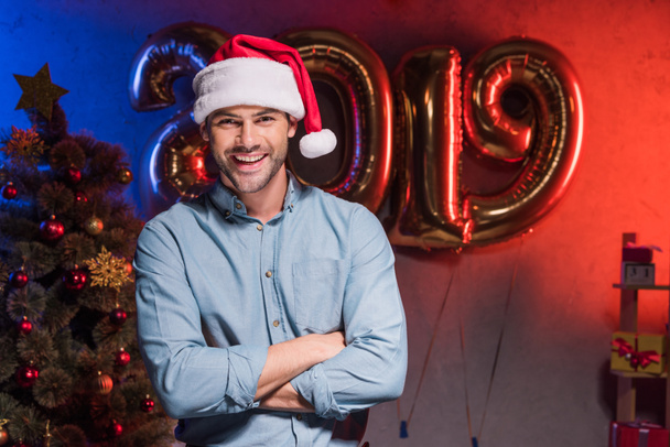 handsome businessman in santa hat standing with crossed arms at new year corporate party - Foto, imagen
