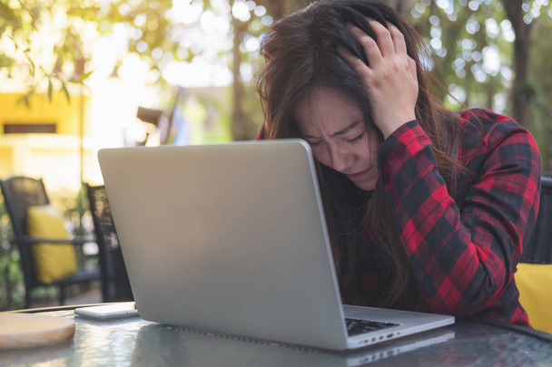 Image rapprochée d'une femme d'affaires asiatique avec un sentiment de stress et de fatigue, fermez les yeux tout en utilisant un ordinateur portable sur une table en verre assis à l'extérieur avec fond vert de la nature
 - Photo, image