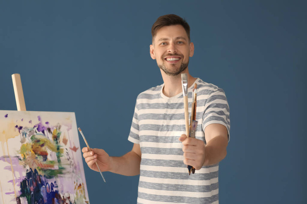 Male artist holding paintbrushes on color background - Фото, изображение