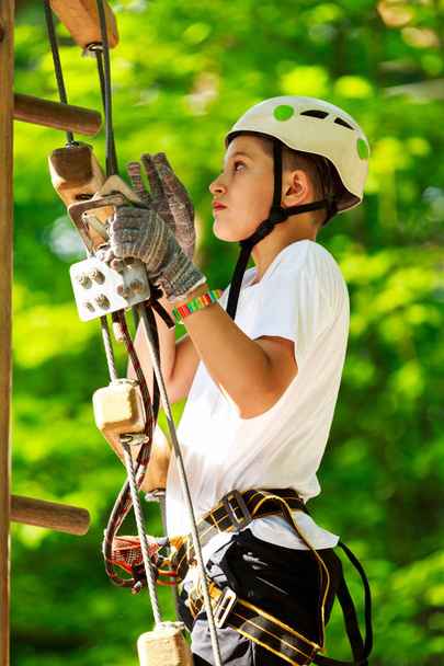 cute, sporty boy in white t shirt in the adventure rope activity park with helmet and safety equipment.Young boy playing and having fun doing activities outdoors. Hobby, active lifestyle concept - Zdjęcie, obraz