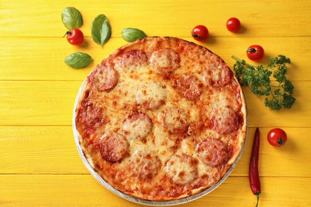 Savoureux pepperoni pizza, tomates et herbes sur fond de bois de couleur
 - Photo, image