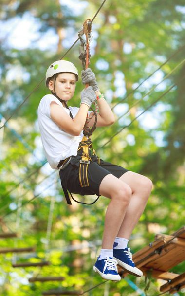 niedlicher, sportlicher Junge in weißem T-Shirt im Abenteuerseilpark mit Helm und Sicherheitsausrüstung. Hobby, aktives Lebensstil-Konzept - Foto, Bild
