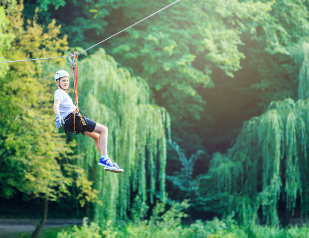 cute, sporty boy in white t shirt and white helmet in the adventure rope activity park with helmet and safety equipment.Young boy playing and having fun doing activities outdoors. Hobby, active lifestyle concept - Photo, Image