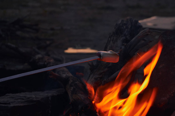 preparation of very tasty sweet dessert of marshmallow on fire of a fire during a rest on a hike in a warm summer evening in nature - Foto, Bild