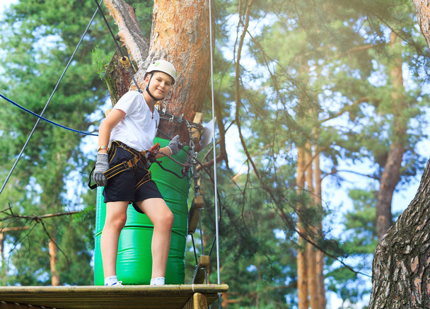 cute, sporty boy in white t shirt in the adventure rope activity park with helmet and safety equipment.Young boy playing and having fun doing activities outdoors. Hobby, active lifestyle concept - Photo, Image