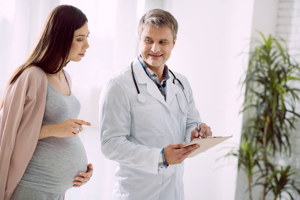 Nice pregnant woman looking at the doctors notes - Фото, зображення