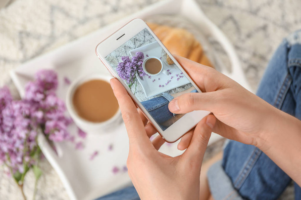 Woman taking photo of blossoming lilac and cup with coffee, closeup - Photo, Image