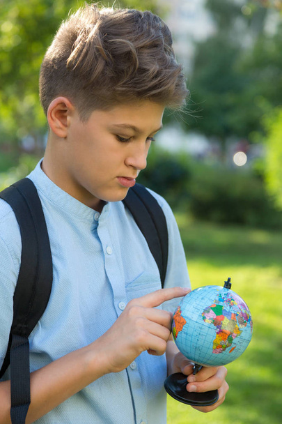 Cute, young boy in blue shirt holds a globe  in his arms in the park in the summer. Back to school, education concept - Photo, Image