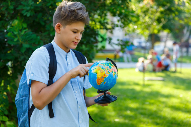 Roztomilý, mladý chlapec v modré košili drží glóbus v náručí v parku v létě. Zpátky do školy, koncepce vzdělávání - Fotografie, Obrázek