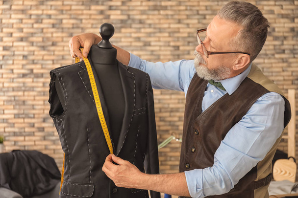Sastre maduro tomando medidas de chaqueta en maniquí en atelier
 - Foto, Imagen