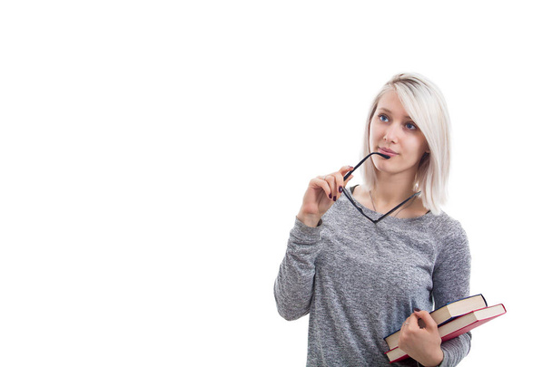 Chica inteligente sosteniendo libros en una mano y anteojos en otra. Estudiante pensante aislado sobre fondo blanco
. - Foto, Imagen