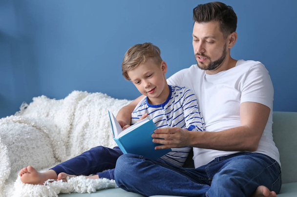 Father and his son reading book together at home - Photo, Image