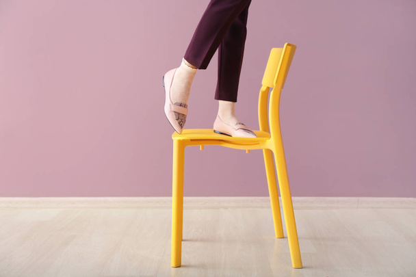 Las piernas de la hermosa mujer joven de pie en la silla contra la pared de color
 - Foto, imagen