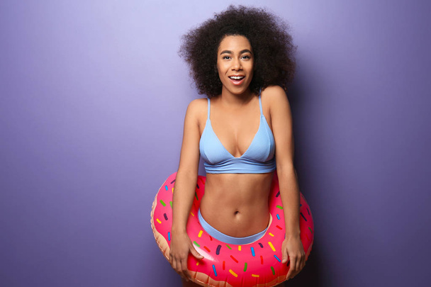 Beautiful African-American woman in bikini and with swim ring on color background - 写真・画像