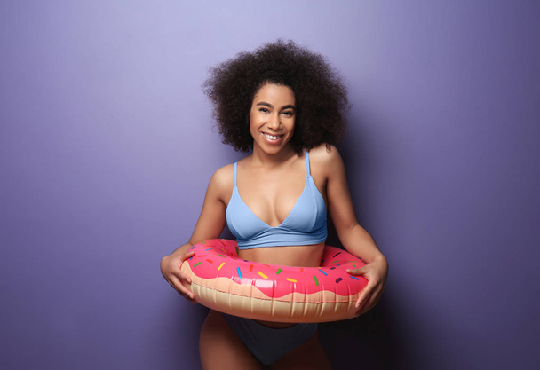 Mooie Afro-Amerikaanse vrouw in bikini en met zwemmen ring op kleur achtergrond - Foto, afbeelding