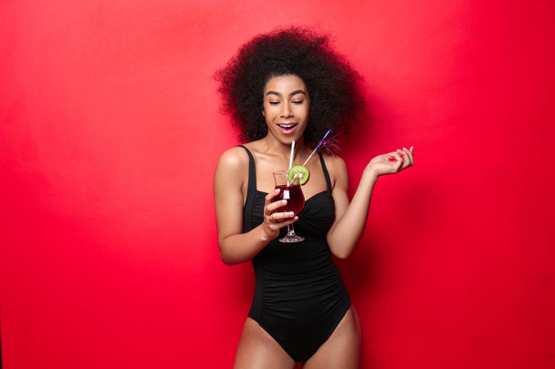Beautiful African-American woman in swimming suit and with tasty cocktail on color background - Foto, imagen
