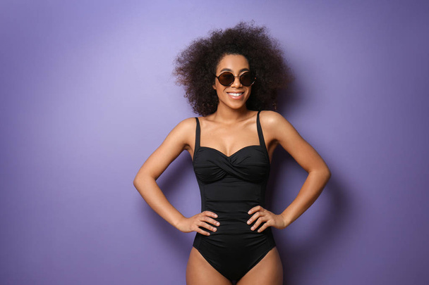 Beautiful African-American woman in swimming suit and with sunglasses on color background - Foto, Imagen