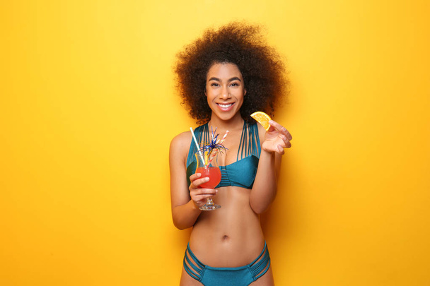 Beautiful African-American woman in bikini and with tasty cocktail on color background - Photo, image