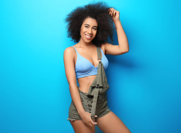 Mooie Afro-Amerikaanse vrouw in bikini en jumpsuit op kleur achtergrond - Foto, afbeelding