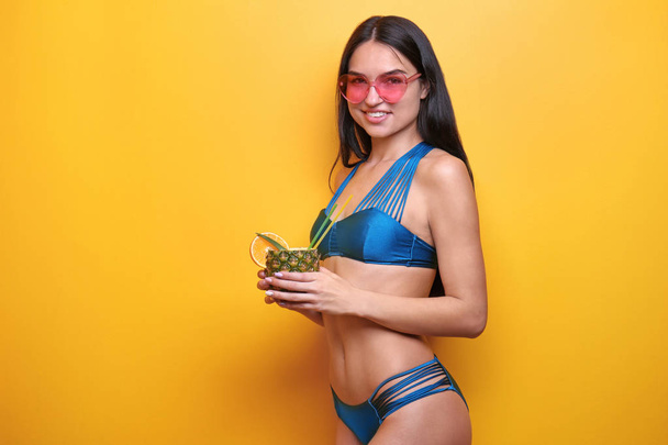 Hermosa mujer joven en bikini con bebida y gafas de sol sobre fondo de color
 - Foto, Imagen