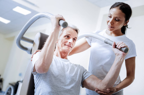 Enthusiastic pensioner using exercise equipment in a rehabilitation center - Foto, Imagem