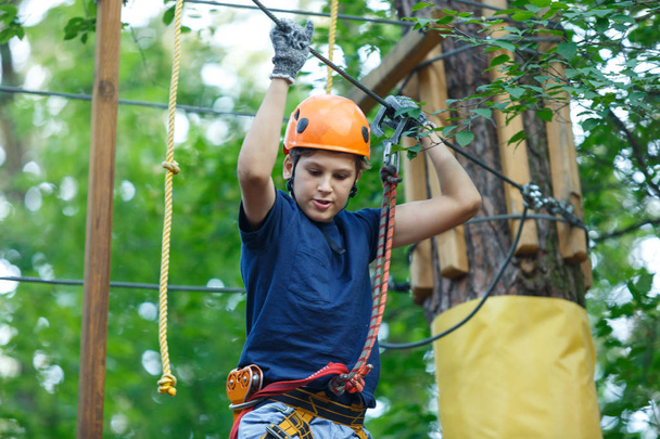 Feliz, bonito, menino em azul t-shirt e capacete laranja se divertindo e jogando no parque de aventura, segurando cordas e subir escadas de madeira. conceito de estilo de vida ativo
 - Foto, Imagem