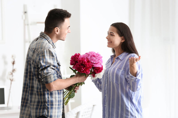 Young man giving beautiful flowers to his beloved girlfriend indoors - Фото, зображення