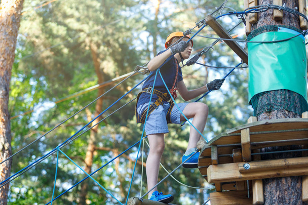 Happy, cute, young boy in blue t shirt and helmet having fun and playing at adventure park, holding ropes and climbing wooden stairs. active lifestyle concept - Photo, Image