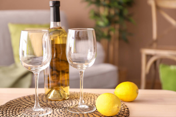 Wooden table with glasses, bottle of wine and lemons in living room - Foto, afbeelding