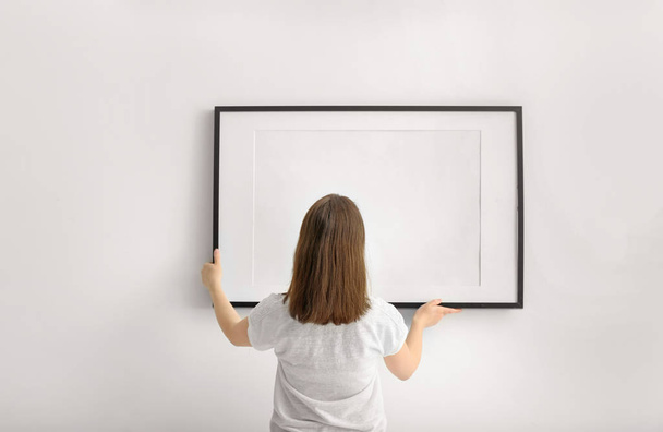 Woman hanging blank photo frame on white wall - Foto, afbeelding