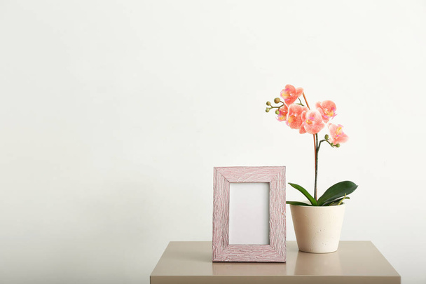 Blank photo frame and houseplant on table against white wall - Foto, imagen