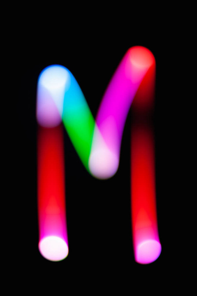 Letter M. Glowing letters on dark background. Abstract light painting at night. Creative artistic colorful bokeh. New Year. Use it for build you own design for book cover, CD, poster or post card. - Photo, Image