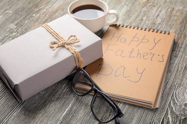 Gift box with cup of coffee. eyeglasses and notebook on wooden background. Happy Father's Day - Photo, Image