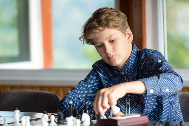 lindo, chico inteligente con camisa azul se sienta en el aula y juega al ajedrez en el tablero de ajedrez. Formación, lección, afición, concepto de educación. intelectual juego
 - Foto, Imagen