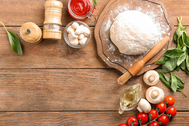 Composition with raw dough and ingredients for pizza on wooden background - Photo, Image