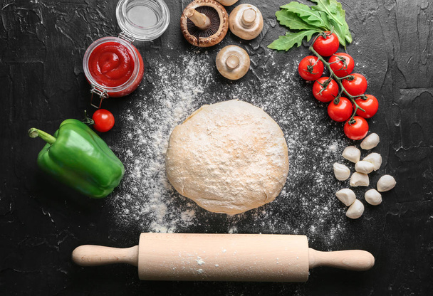 Composición con masa cruda e ingredientes para pizza sobre fondo texturizado
 - Foto, Imagen