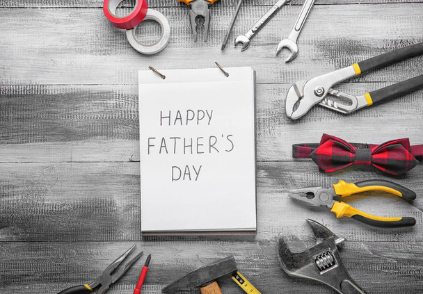 Cuaderno con texto "Feliz Día del Padre", pajarita y juego de herramientas sobre fondo de madera
 - Foto, imagen