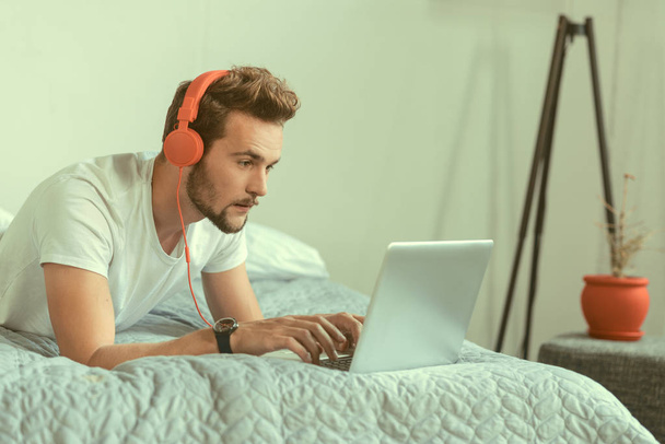 Concentrated guy wearing headphones working on laptop - Fotó, kép