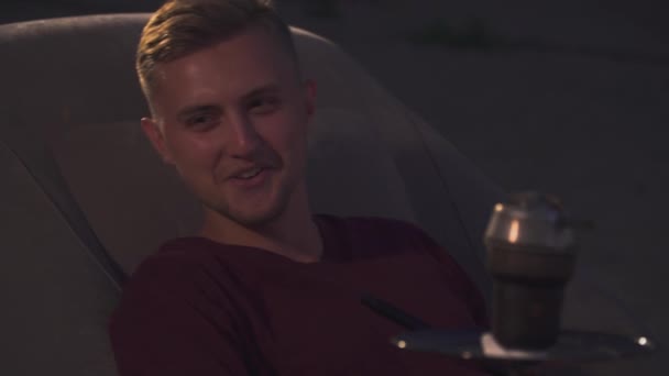 Young man sits in an armchair next to a hookah - Video