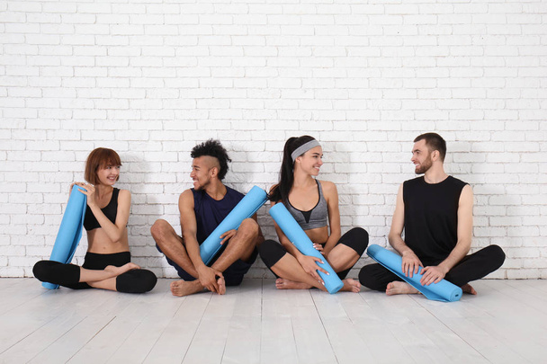 Group of sporty people with yoga mats sitting near white brick wall - Foto, Imagen