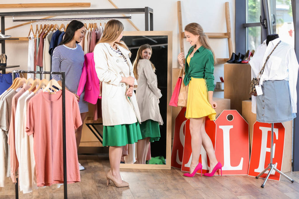 Jonge mooie vrouwen kleren in moderne winkel kiezen - Foto, afbeelding